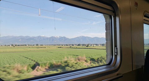 La vue depuis la fenêtre d'un train sur des champs verts et des montagnes lointaines